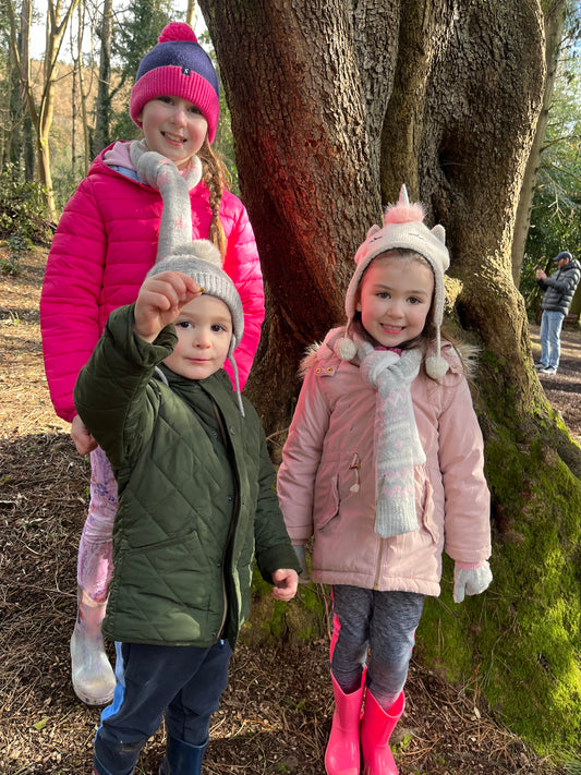 Two children standing under a large tree in a forest setting