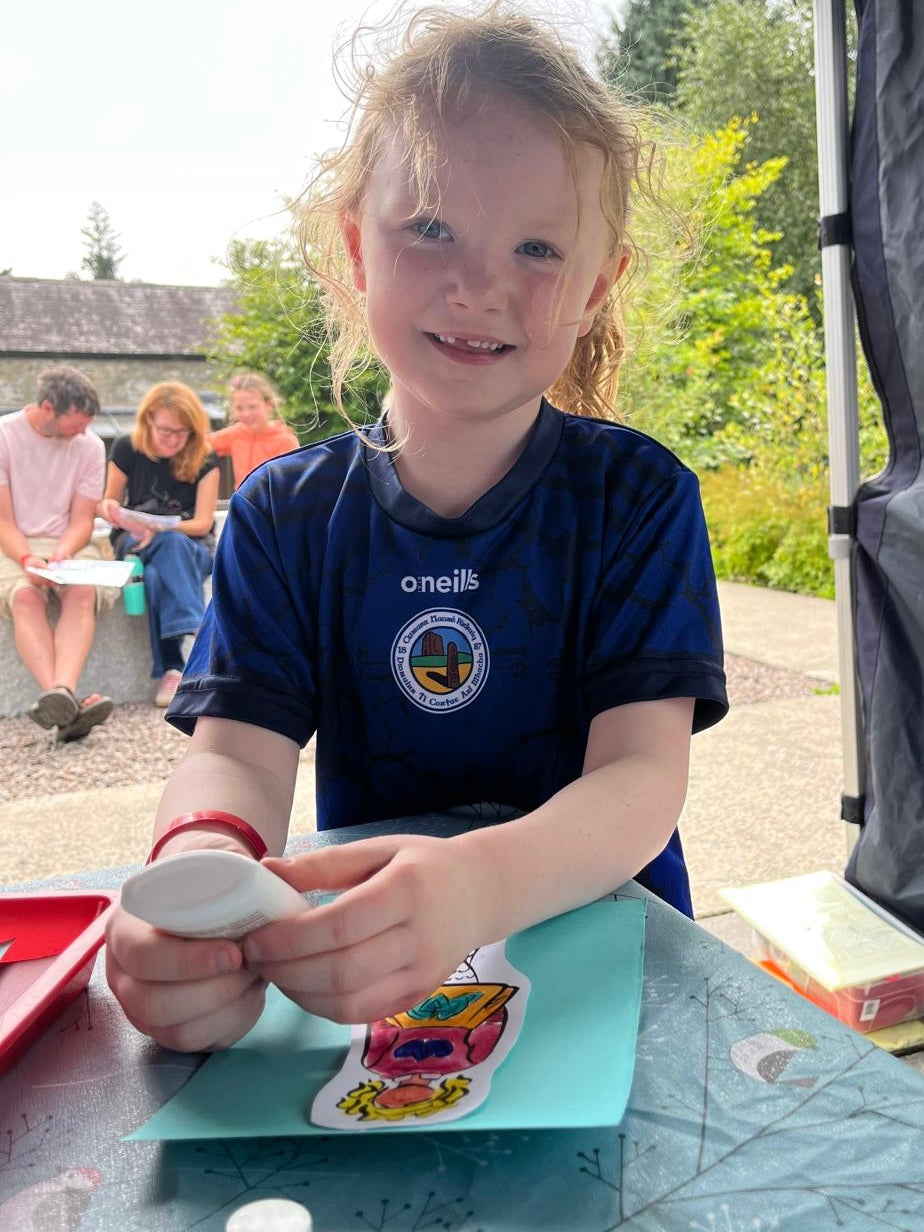 Child sitting at a table outdoors with family in the background creating art