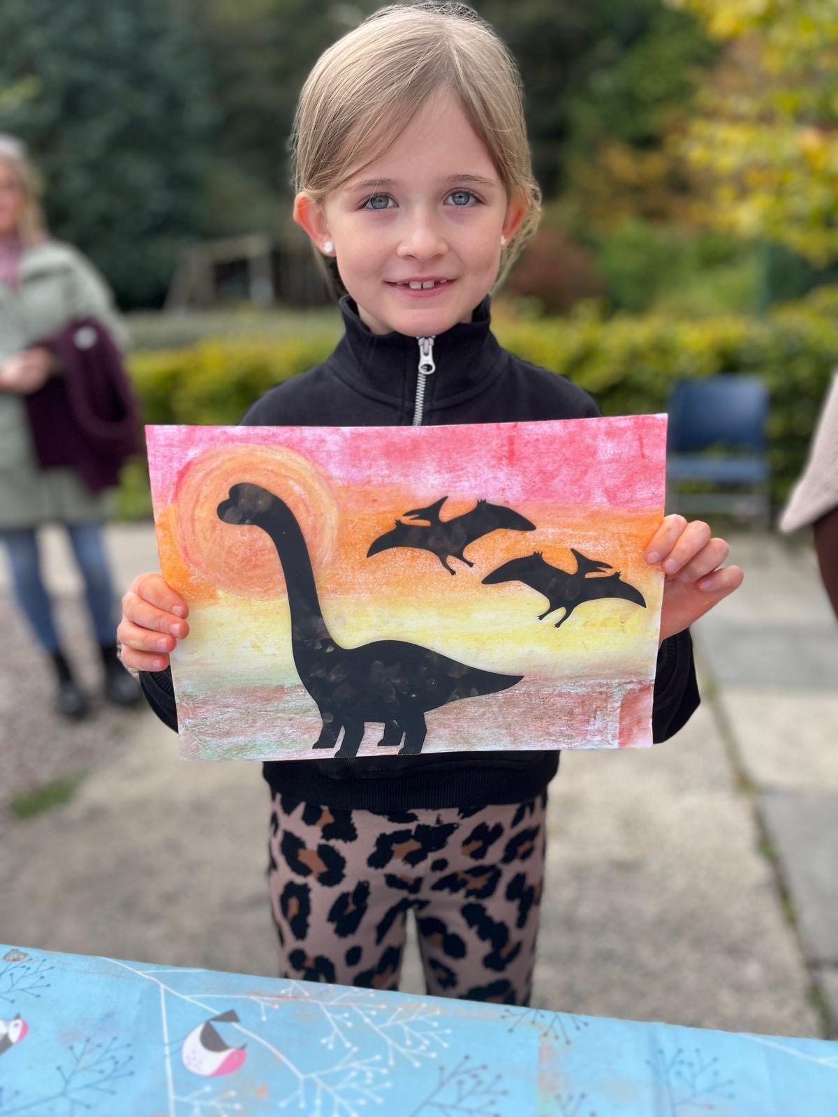 Child holding a painting of a dinosaur silhouette against a sunset sky