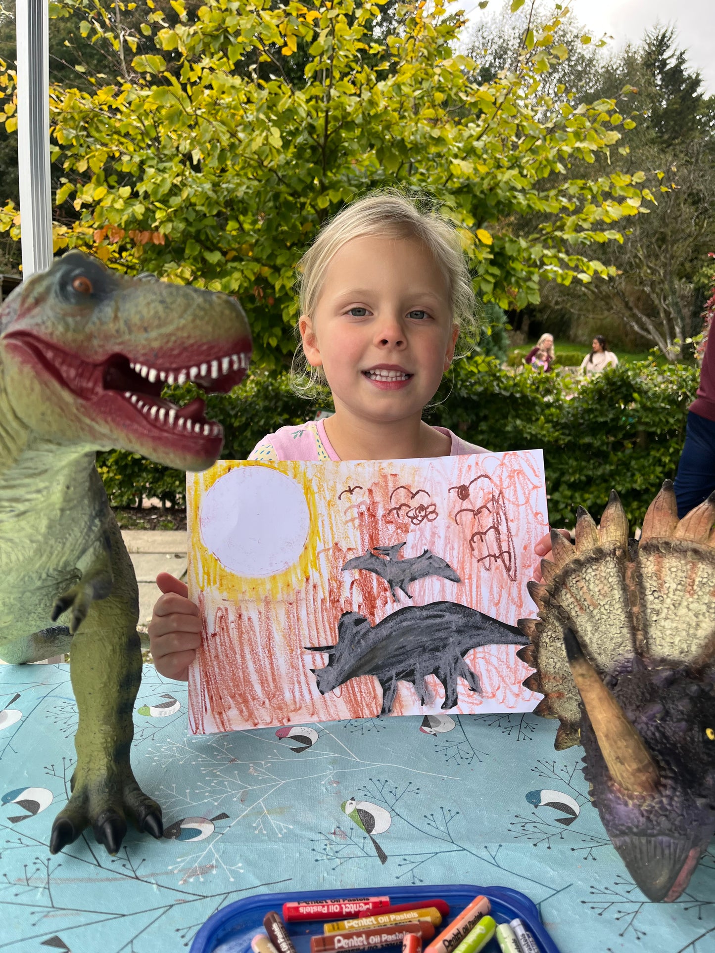 Child holding a drawing of a dinosaur with large toy dinosaurs in the foreground.